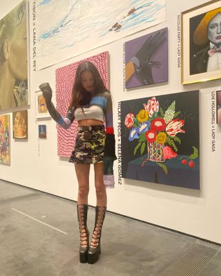 Olivia Rodrigo wearing black knee-high platform Mary Janes, camo skirt, and crop top.