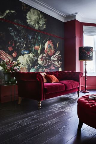 A painted floral mural in a dark living room with red velvet upholstered sofa