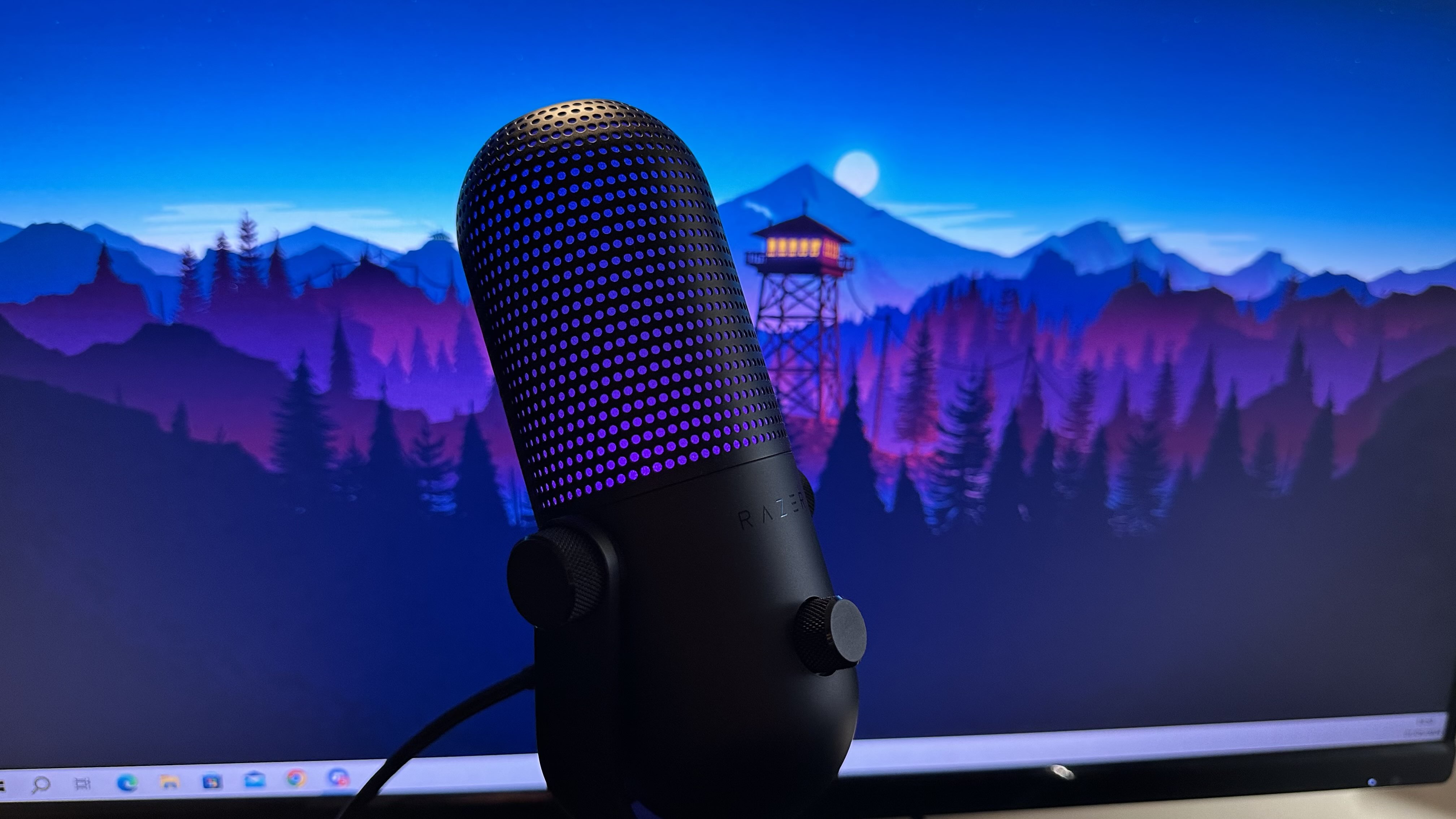 Razer Seiren V3 Chroma review image of the mic with purple lighting in front of a Firewatch wallpaper