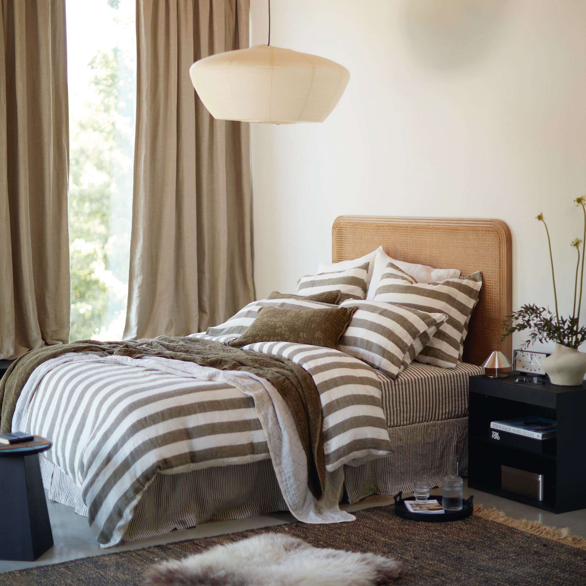 White bedroom with rattan headboard, white and brown stripe bedding with large white lampshade.