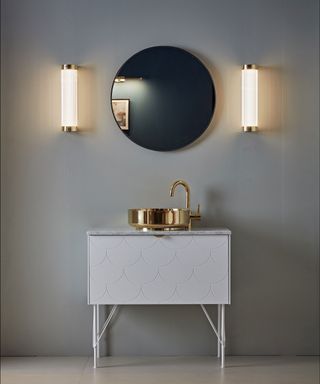 Two LED lights on either side of a round mirror above a gold sink