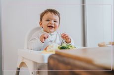 A baby eating food while sat in a high chair