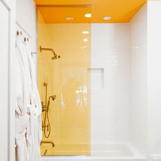 Bathroom with yellow ceiling, chrome shower attachments and robes hanging on the wall