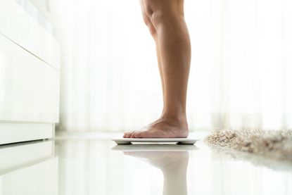 A close-up of a woman in the bathroom on her scales at the best time to weigh yourself