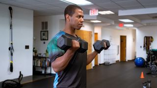 Man performs dumbbell curls in empty gym