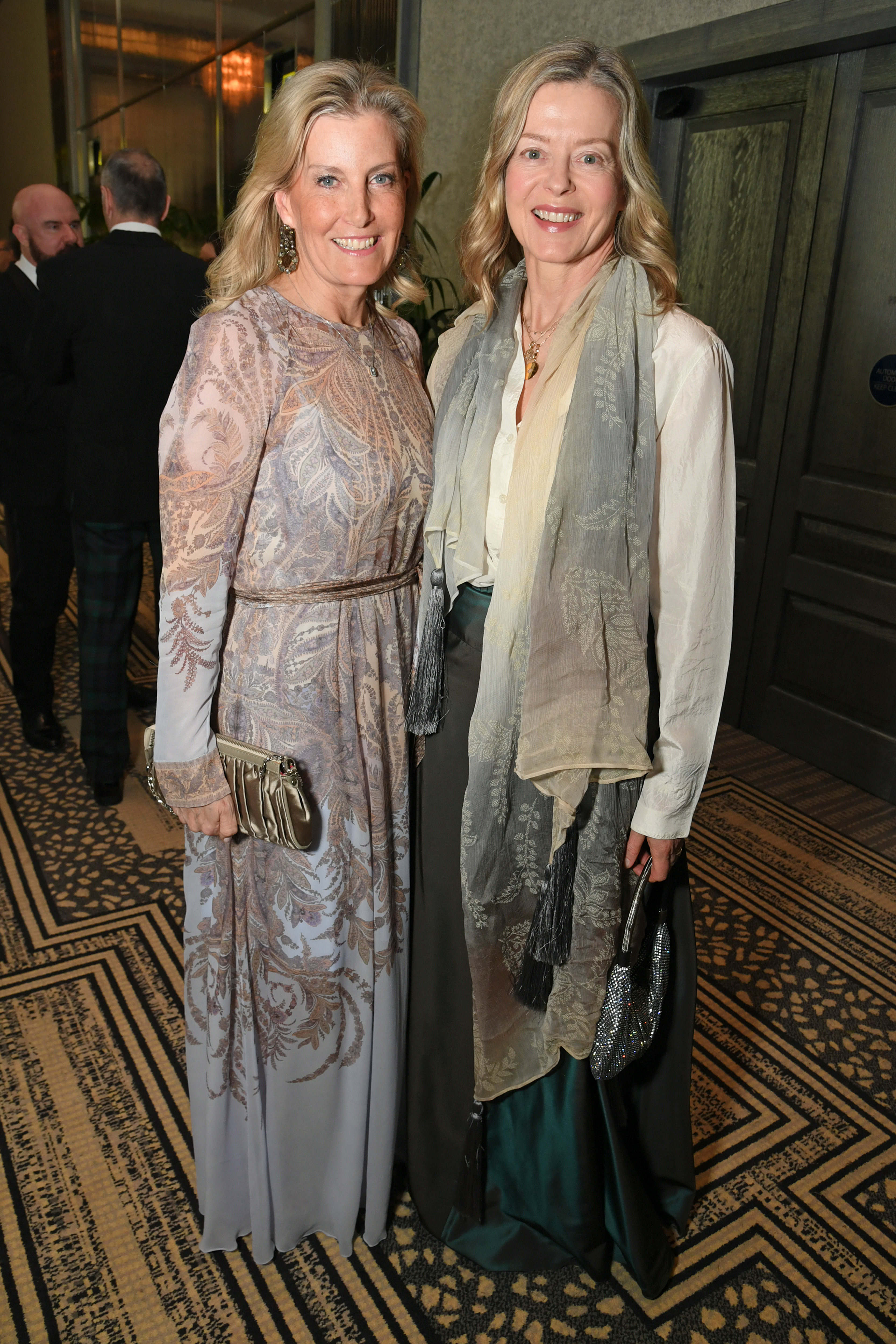 Duchess Sophie wearing a sheer blue paisley dress and smiling next to Lady Helen Taylor