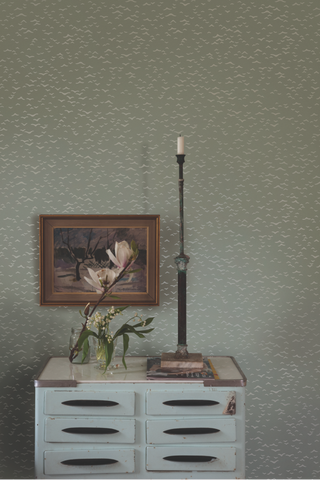 Green fine print wallpaper in hallway with industrial cabinet, black vintage candle stick holder and frame on the wall