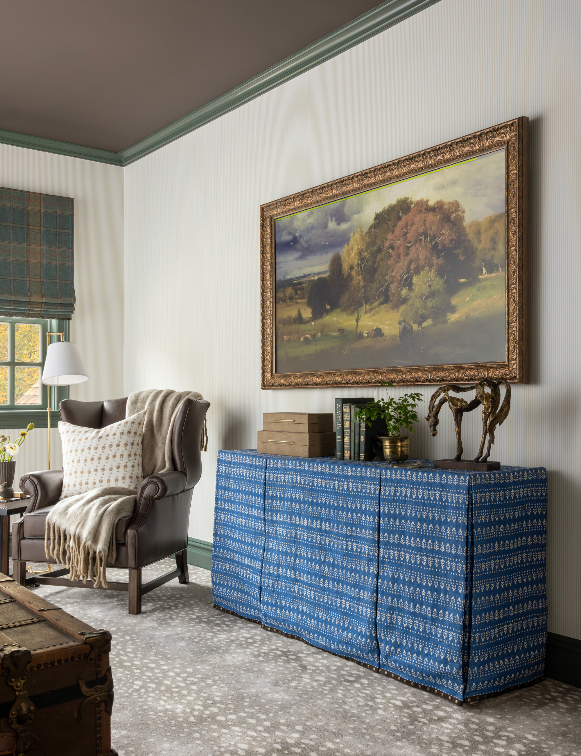 Equestrian-inspired living room featuring a rustic leather armchair, ornately framed wall art, and a textile-covered credenza topped with a horse-motif statue