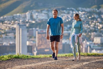 Fitness, morning and couple in city walking for exercise, cardio workout and training together. Marriage, happy and mature man and woman on hill for wellness, health and wellbeing in urban town