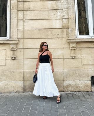 Woman wears black strappy top, white maxi skirt and black strappy sandals