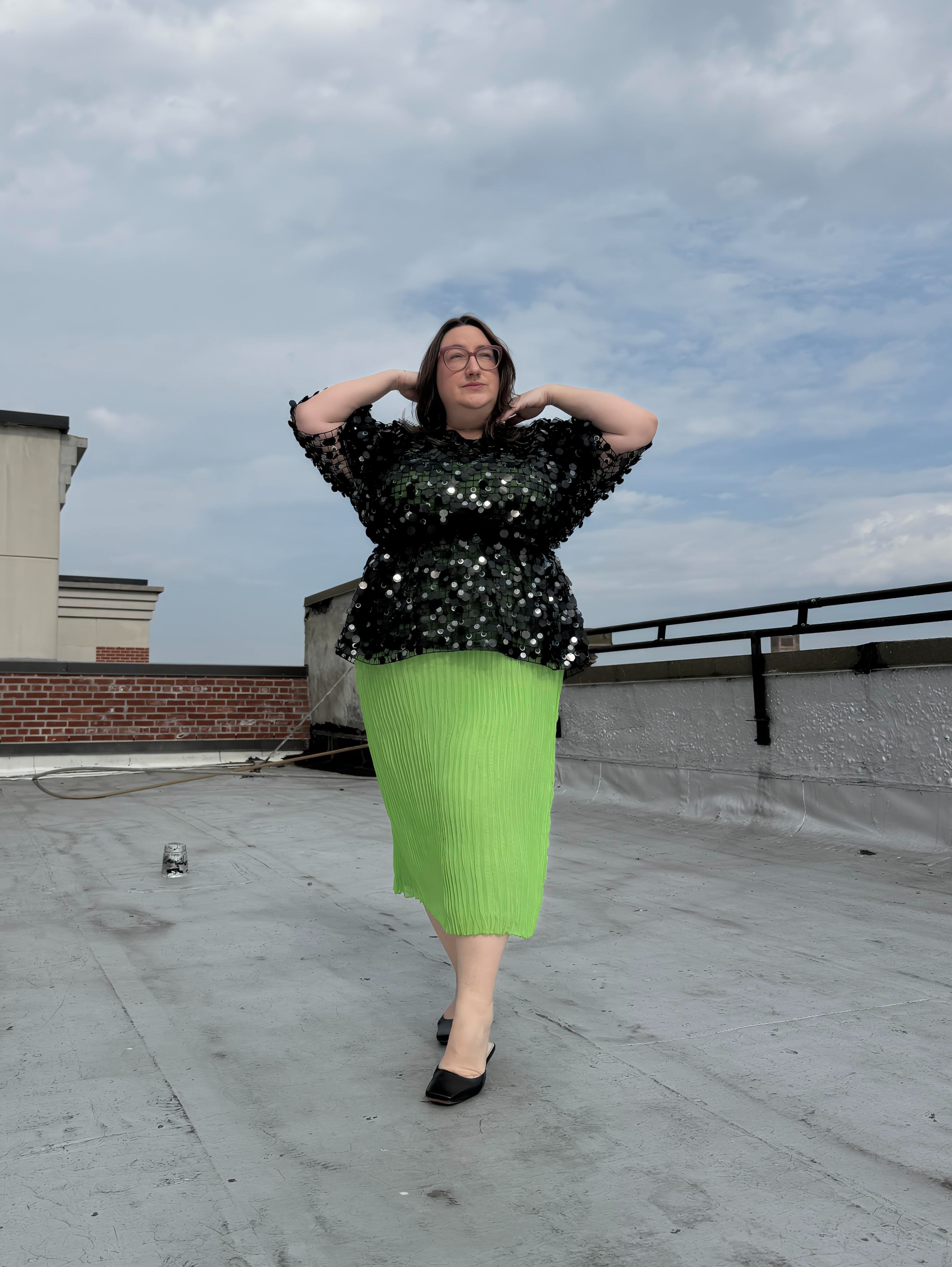 Sarah Chiwaya poses in a paillette-embellished peplum top layered over a lime green pleated skirt