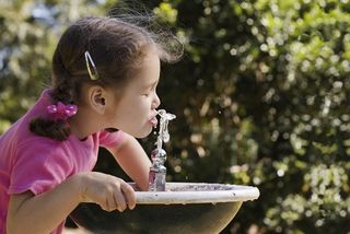 Young girl drinking water from a water fountain.