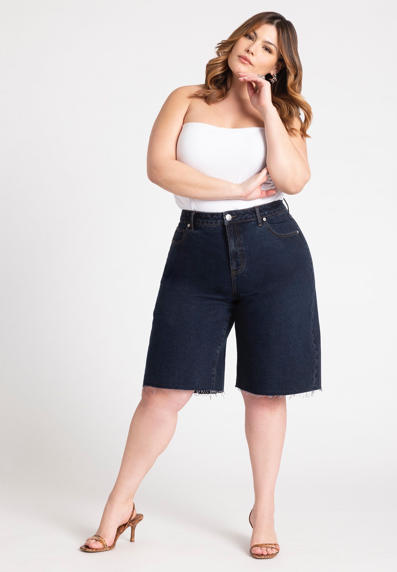 model wears dark long denim short and white top with a brown heel