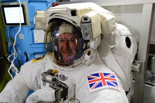 a man sits in a spacesuit with a british flag patch on teh shoulder.