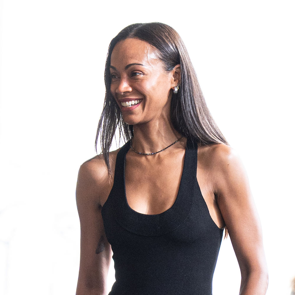 Zoe Saldana wearing a black tank top, bermuda shorts, and black flats