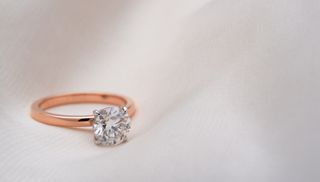 A rose gold diamond ring on a cream, fabric background.