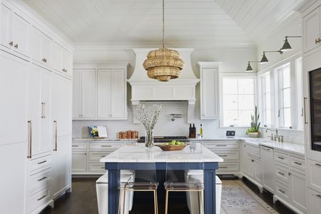 white kitchen with blue kitchen island, wicker pendant light, shiplap ceiling, wall lights, dark wooden floor, rug