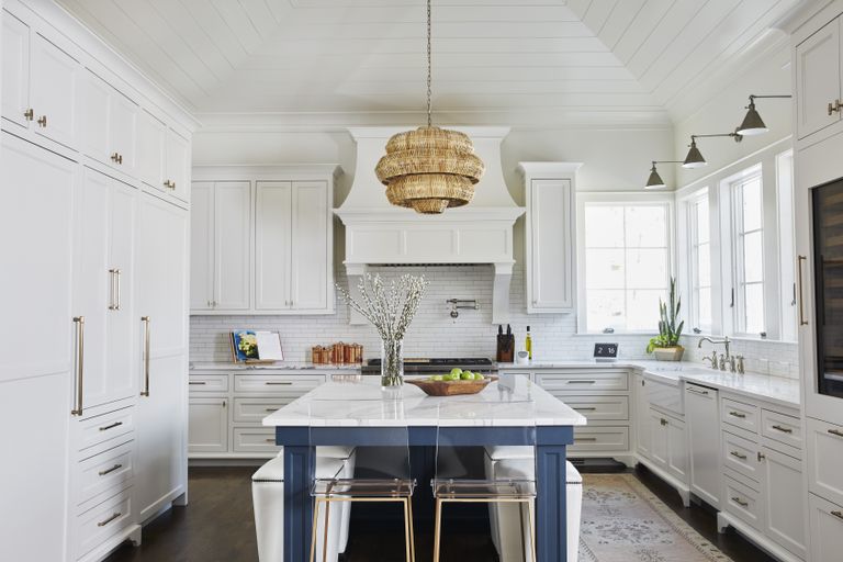 white kitchen with blue kitchen island, wicker pendant light, shiplap ceiling, wall lights, dark wooden floor, rug