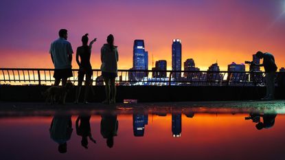 People watch a summer sunset across the harbor in New York City.