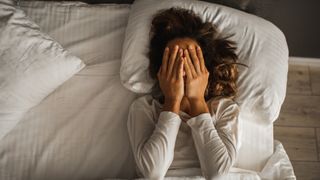 Woman lying in bed with hands over her face, unable to sleep