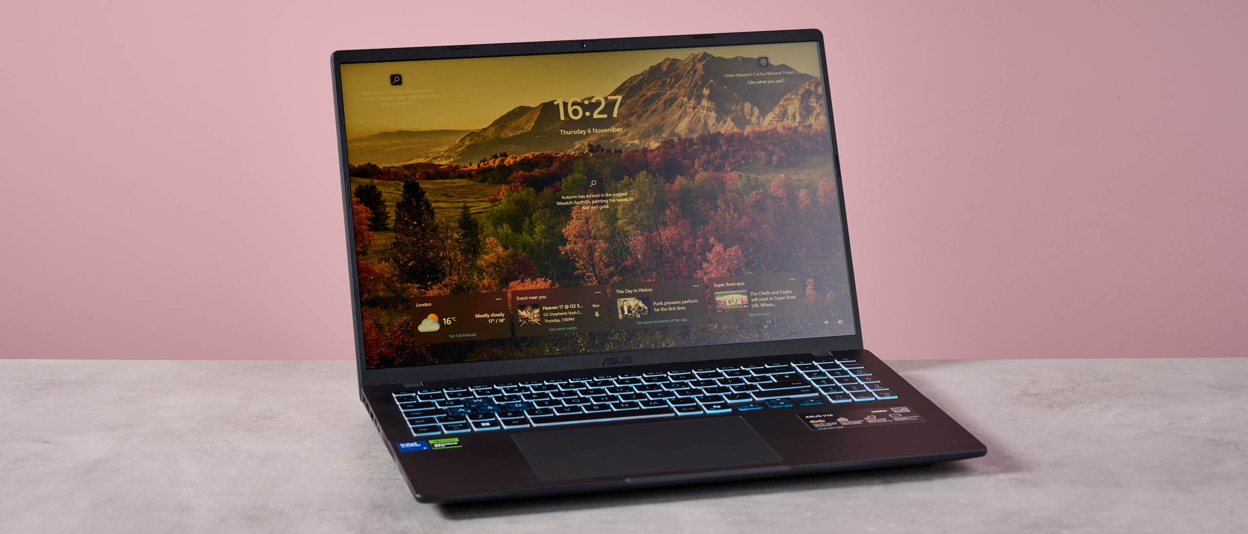 Three-quarter view of Asus V16 open on desk with pink wall in background