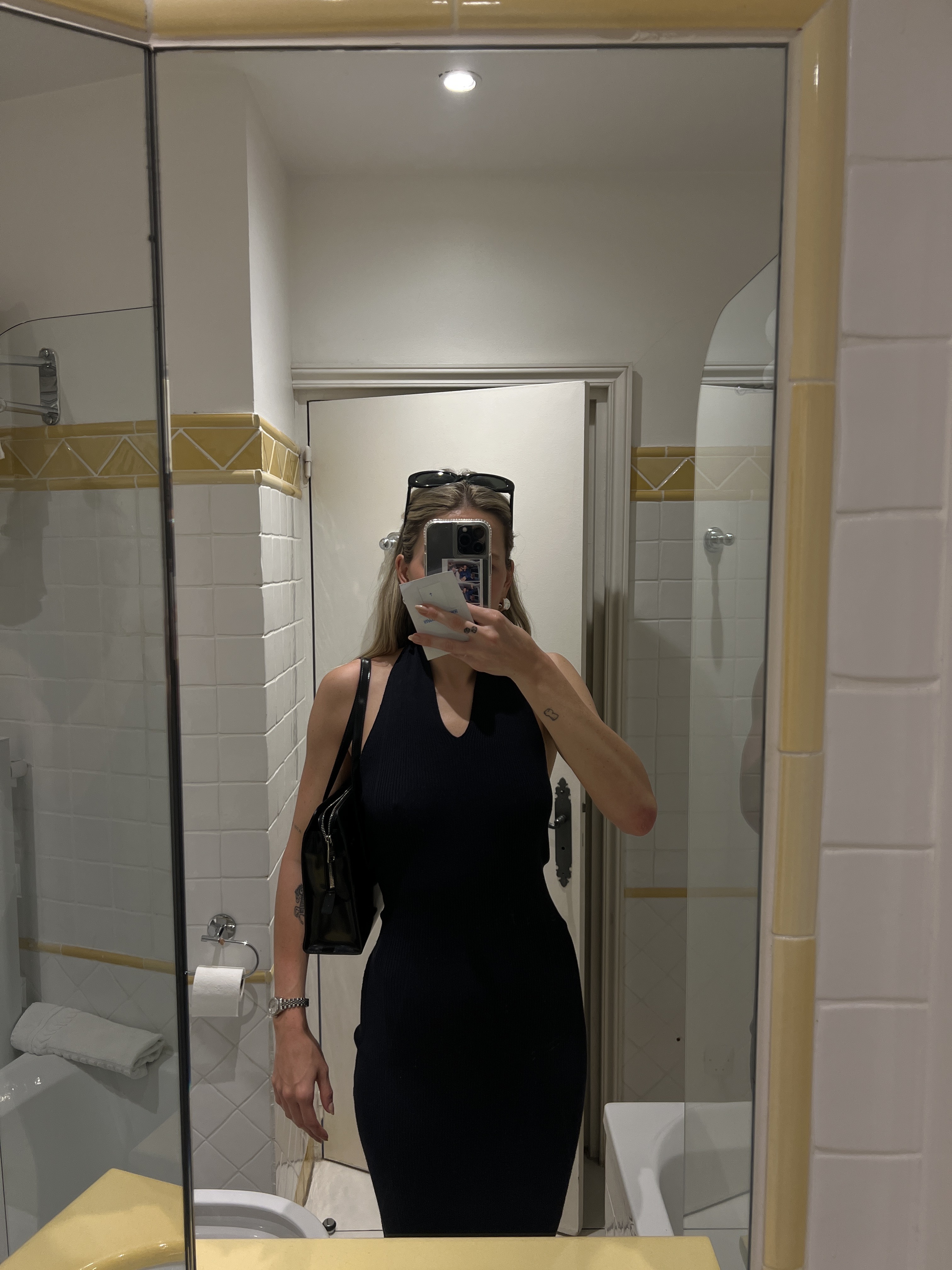 Eliza Huber in a mirror selfie wearing a navy blue halter dress with a black bag and sunglasses.