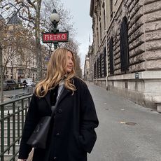 olivia wears black coat while posing on the streets of paris