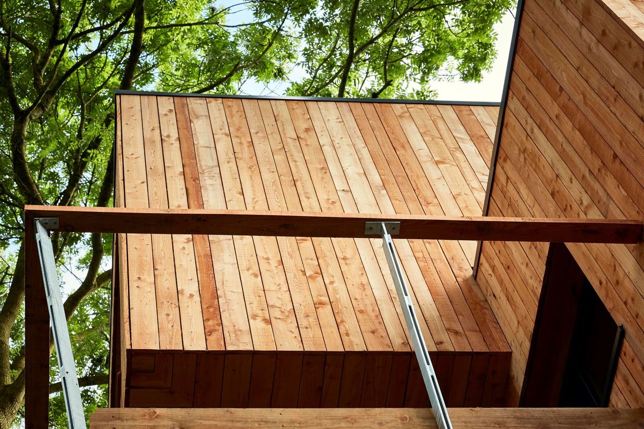 The exterior of the house is made of tall wooden panelling with the house including different levels separated by a balcony