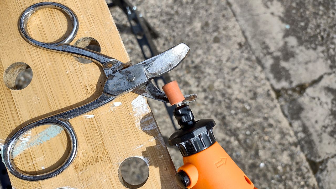 An orange rotary multi tool being used to sharpen a pair of scissors