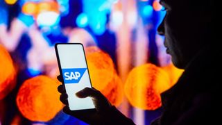 A person silhouetted by lights holds a smartphone with the SAP logo displayed