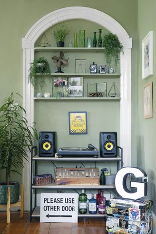 Alcove in living room with green painted walls, shelving containing vases, frames and plants, and record player and speaker