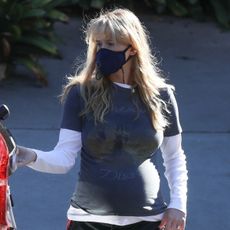 Jennifer lawrence wears a mask, white long-sleeve shirt, graphic t-shirt, and black adidas track pants.