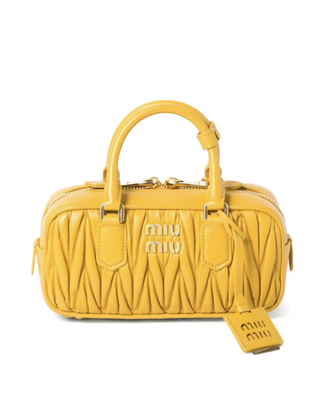 a yellow quilted miu miu bag in front of a plain backdrop