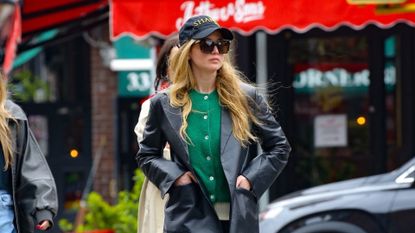 Jennifer Lawrence walking in the street wearing track pants, a green cardigan, and leather blazer.