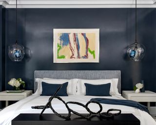 A master bedroom demonstrating apartment bedroom ideas with navy gloss painted walls and statement artwork, including a sculpture at the end of the bed