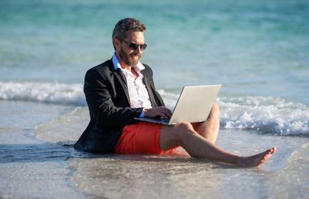Freelancer business man on summer vacation. Summer weekend and remote freelance work. business man with laptop. Business man dreams on summer in sea. Summer business. Fun lifestyle.