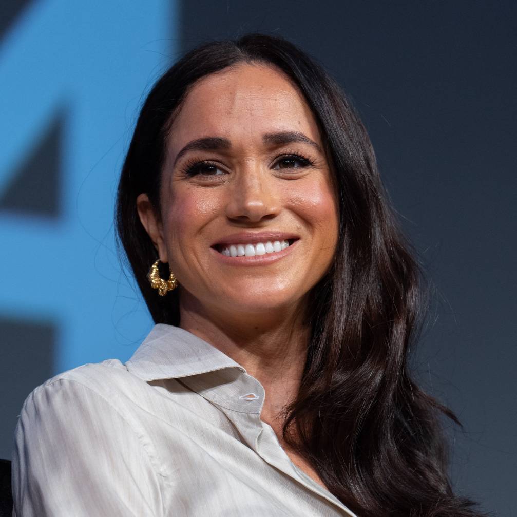 Meghan Markle smiles in front of a blue background