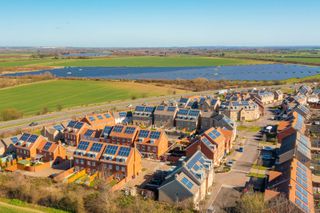 A housing estate viewed from above with solar panels on roofs visible plus a solar farm in the background