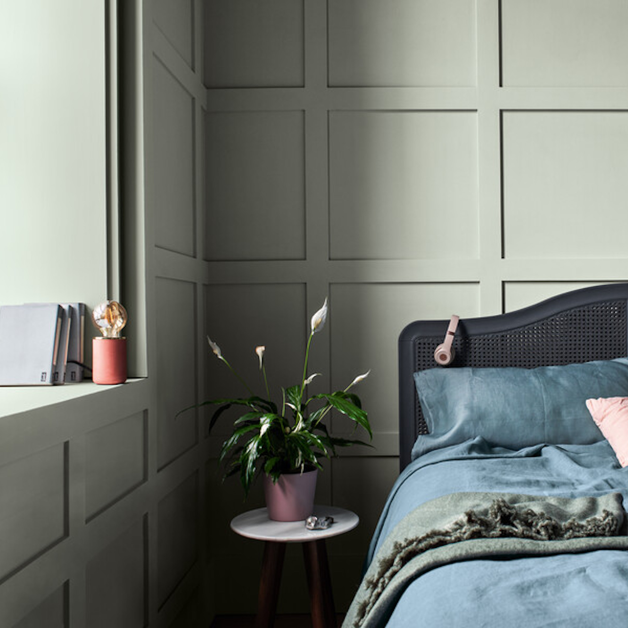 bedroom drenched in pale green paint with wall panelling and bed with blue bedding