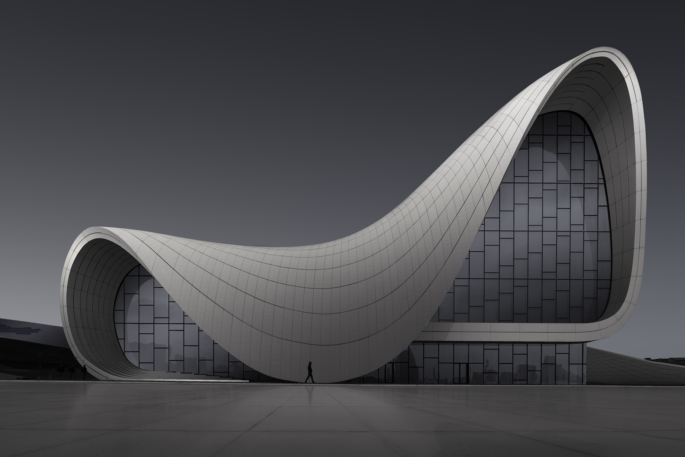 A modern, curvilinear building with a sleek, futuristic design, featuring large glass windows and a minimalist exterior against a dark sky