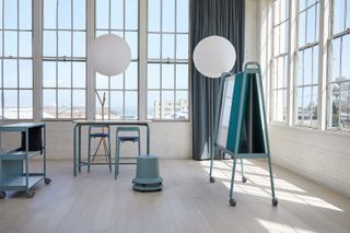 A storage trolley, tall desk and chairs, stacked stools and work screen, all in teal, part of the ‘Routes’ collection of office furniture designed by Pearson Lloyd for Teknion