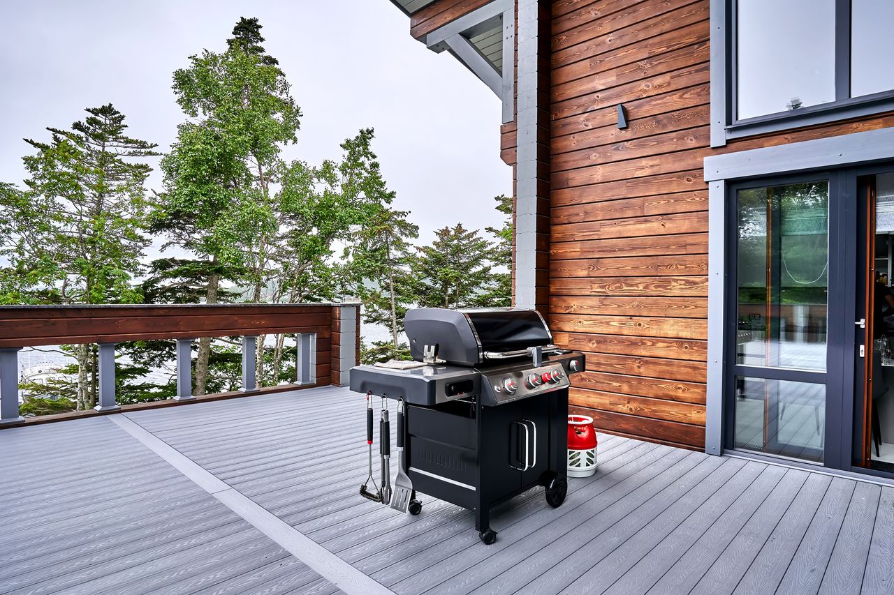 Grill on the outdoor terrace of a wooden house with a view of the forest and lake