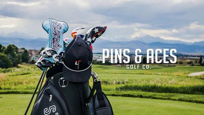 A golf caddy full of clubs stood on a green hill with the Pins and Aces logo and white text next to it