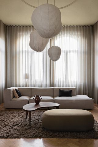 Ένα ελαφρύ μοντέρνο σαλόνι με διάφανες κουρτίνες, μεγάλο καναπέ, τραπεζάκι και μεγάλου μεγέθους πουφ