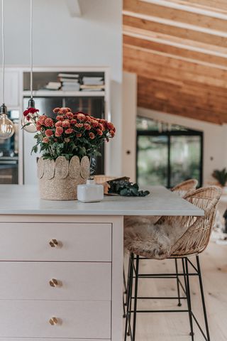 A pretty pale pink kitchen with brass handles and rustic vase of flowers