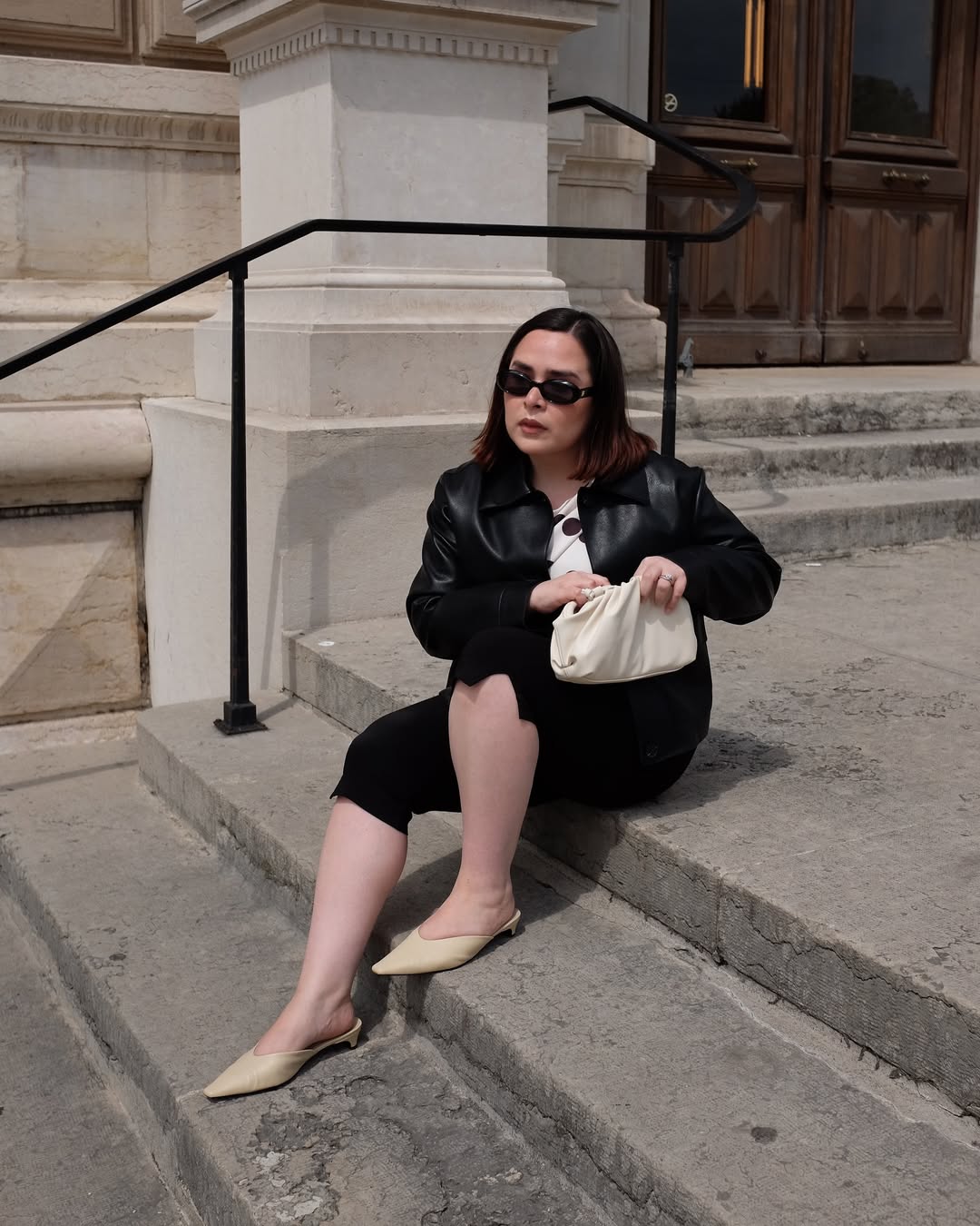 @indiraci wears pale yellow mules with a polka dot top, black capri pants, black leather bomber jacket and white clutch