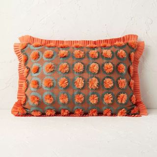 An orange, green, and brown fringe and pom throw pillow is one of the best Target fall decor items.