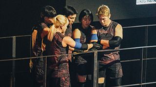 a team of five contestants strategize before a challenge, in 'physical: 100' season 2