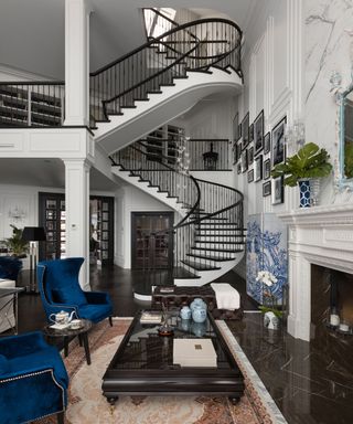 Large, elegant family sitting room, spiral staircase up three floors, two blue armchairs, ottoman, fireplace