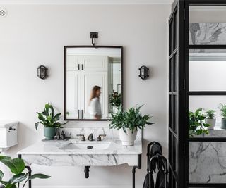 white bathroom with black taps, shower frame and green plants dotted around